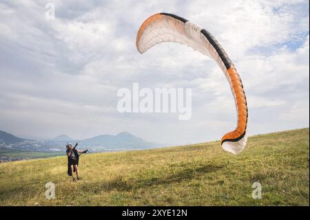 Der Gleitschirmflieger öffnet seinen Fallschirm, bevor er vom Berg im Nordkaukasus abhebt. Füllen Sie den Fallschirmflügel vor dem Start mit Luft Stockfoto