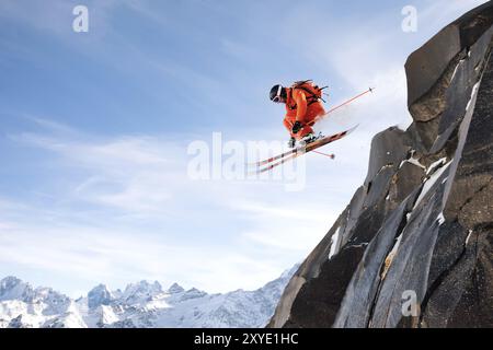 Ein professioneller Skifahrer macht einen Sprung von einer hohen Klippe gegen den blauen Himmel und hinterlässt eine Spur aus Schneepulver in den Bergen. Kaukasischer Kamm im Stockfoto