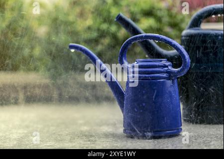 Zwei kleine Gießkannen auf dem Balkon bei strömendem Regen Stockfoto