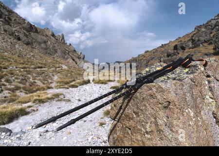 Professionelle Sticks zum Besteigen eines Berges in der Nähe eines Steines auf einem hohen Bergweg vor blauem Himmel und weißen Wolken. Das Konzept der aktiven Erholung Stockfoto