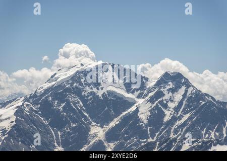 Ein dunkelblauer Himmel mit Wolken auf den felsigen Gipfeln von Bergen, die mit Gletschern und Schnee im Kaukasus bedeckt sind Stockfoto