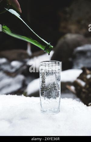 Reines Mineralwasser wird aus einer glasgrünen Flasche bis zum letzten Tropfen in ein klares Glasbecher gegossen. Den Tropfen in der Flasche zu beobachten Glass steht rein Stockfoto