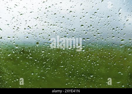 Natürlicher Hintergrund fällt auf beiden Seiten des Glases aus dem Regen und aus der nebelnden abstrakten Ansicht, Regentropfen auf das blaue Glas und die Unschärfe Stockfoto