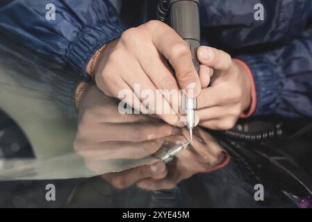 Nahaufnahme von Autoverglasungsarbeitern, die eine Windschutzscheibe oder Windschutzscheibe eines Autos an einer Werkstattwerkstatt reparieren und reparieren. Bohren Sie das Glas für die Reparatur Stockfoto