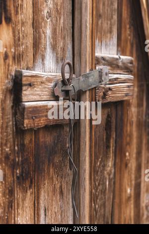 Nahaufnahme altes einfaches Schloss an einer Holztür geschlossen mit einem Metallstift rustikale Verriegelung an einer alten Tür aus Holz, um niemanden mit einem rostigen Metallschloss reinzulassen Stockfoto