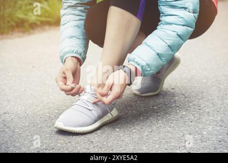 Läuferin, die Schnürsenkel bindet, um ihre Schuhe auf der Straße im Park zu joggen. Laufschuhe, Schnürsenkel. Übungskonzept. Sportlicher Lifestyle. Vintage-Style Stockfoto