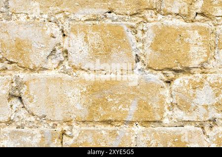 Nahaufnahme strukturierter Hintergrund eines mehrfarbigen, gelb gemalten Ziegels. Eine brutzelnde gelbe Farbe auf einem alten, kaputten Ziegelstein. Grunge-Style Stockfoto