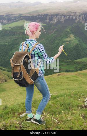 Ein Hipster-Mädchen reiste von einem Blogger in einem karierten Hemd und mit mehrfarbigen Haaren mit einem Kompass, der auf einem Hochplateau in den Bergen stand Stockfoto