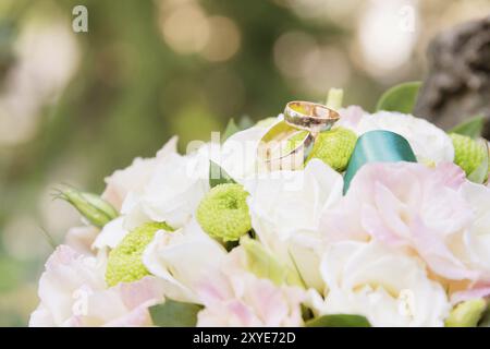 Hochzeitsgoldringe liegen auf einem Hochzeitsstrauß, der aus blauen violetten und weißen Blumen besteht Stockfoto