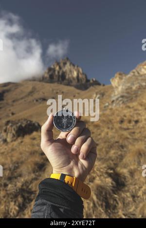 Ein männlicher Wanderer sucht im Herbst eine Richtung mit einem magnetischen Kompass in den Bergen. POV-Aufnahme. Die Hand eines Mannes mit einem Uhrenarmband Stockfoto