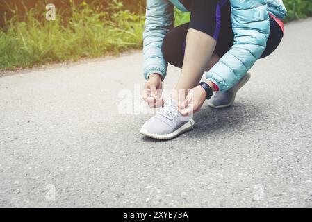 Läuferin, die Schnürsenkel bindet, um ihre Schuhe auf der Straße im Park zu joggen. Laufschuhe, Schnürsenkel. Übungskonzept. Sportlicher Lifestyle. Vintage-Style Stockfoto