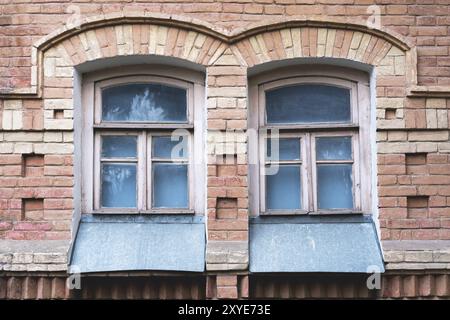 Zwei alte Bogenfenster in einer Wand aus gelben Ziegeln. Grün, die Farben von Meereswellen-Glas in einem braunen dunkelroten Holzrahmen. Das Konzept des antiken V Stockfoto