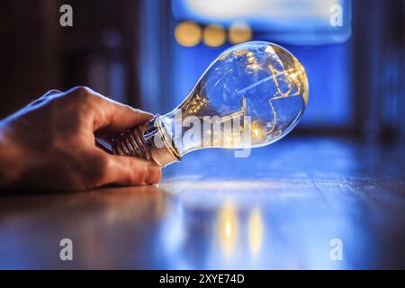 Hände halten eine LED-Glühbirne über dem Holzboden. Symbol für Ideen und Innovation. Fenster und Licht im unscharfen Hintergrund Stockfoto