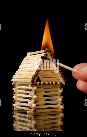 Hand mit einem brennenden Streichholz, das ein Haus in Brand setzt. Spiel mit Streichhölzern, Sachversicherung, Risiko in der Investition, Notfallkonzept. Isolierte Silhouette Stockfoto