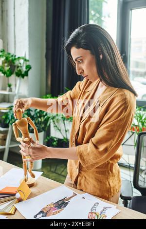 Eine Frau aus dem Nahen Osten arbeitet an einem Modedesign-Projekt in ihrem Büro und positioniert sorgfältig eine hölzerne Schaufensterpuppe, um ihre Arbeit zu inspirieren. Stockfoto