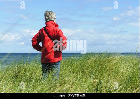 Eine Frau steht in den Dünen und blickt aufs Meer Stockfoto