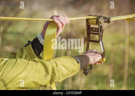 Die Nahhand Eines Mannes passt das Slacklining der Ausrüstung an, bevor er verrückte Slackliner-Tricks ausführt und in einem Park im nat auf einem Slacklin läuft Stockfoto