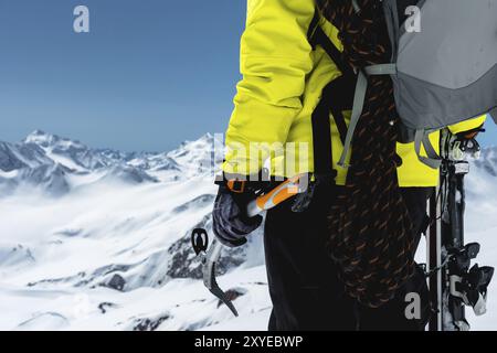 Ein Bergsteiger hält eine Eisaxt hoch in den Bergen, die mit Schnee bedeckt sind. Nahaufnahme von hinten. Outdoor-Klettersport im Freien mit mountai Stockfoto