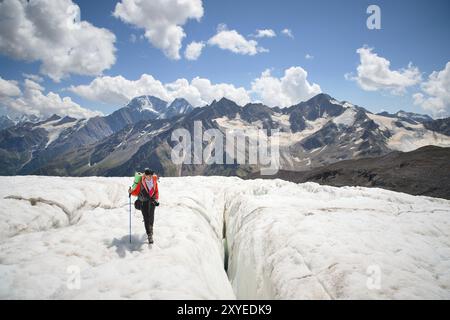 Bergsteigerin genießt die Schönheit des Gletschers Spaziergänge auf dem Gletscher im Steigeisen und in der Sonnenbrille. Vor dem Hintergrund der hohen Berge o Stockfoto