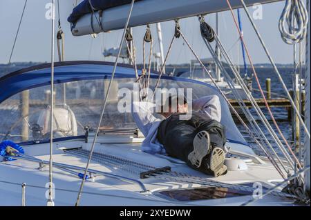 Ein Mann liegt schlafend auf dem Oberdeck einer Segelyacht Stockfoto