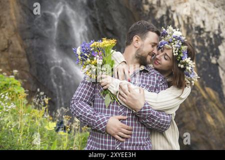 Ein junges Paar verliebter Hipster spazieren durch die Natur vor dem Hintergrund eines Wasserfalls und Bergkräutern und Blumen Stockfoto