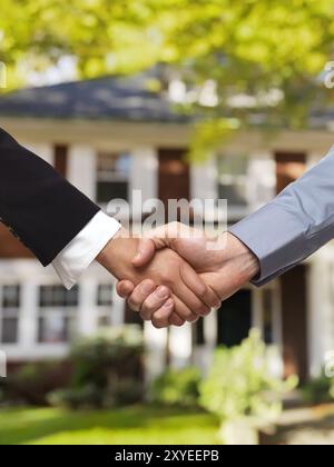 Mann und Frau schütteln vor einem Haus die Hand. Immobilienmaklerkonzept Stockfoto