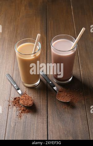 Köstliche Proteinshakes in Gläsern und Löffeln mit Pulver auf Holztisch Stockfoto