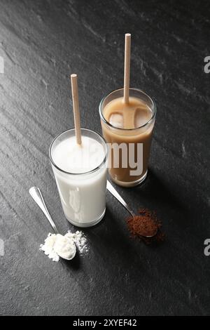 Köstliche Proteinshakes in Gläsern und Löffeln mit Pulver auf schwarzem Tisch Stockfoto