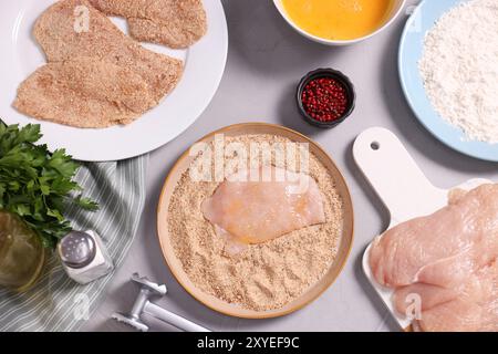 Schnitzel machen. Teller mit roher Fleischscheibe in Semmelbröseln auf grauem Tisch, flach gelegt Stockfoto