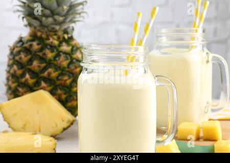 Leckerer Ananas-Smoothie in einmachgläsern und frisches Obst auf dem Tisch, Nahaufnahme Stockfoto