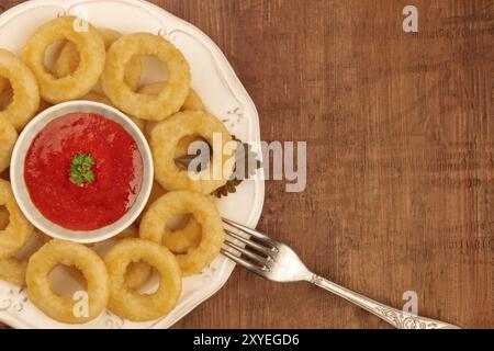 Ein top closeup Schuss Tintenfischringe mit Tomatensauce und eine Gabel auf einem dunklen Hintergrund Stockfoto
