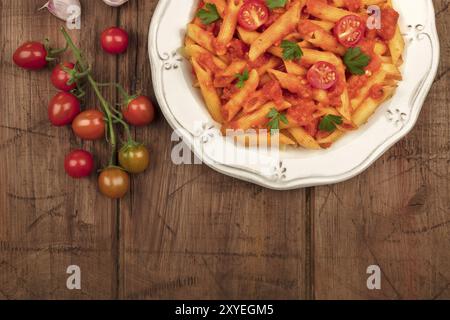 Ein Foto von einem Teller Pasta mit Tomatensauce. Penne Rigate mit Cherry Tomaten und frische Petersilie, auf einem dunklen rustikalen Textur mit einem p Stockfoto