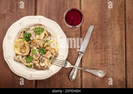 Overhead Foto von scallopine di Vitello, Kalbfleisch scallopini, mit Pilzsauce, Zitronen, und Petersilie, geschossen von oben auf dunklen rustikalen Textur mit Glas Stockfoto