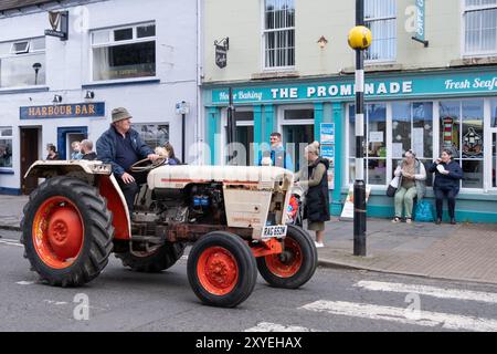 Mann mit Eimerhut, der einen roten David Brown 885 Traktor durch die Stadt fährt. Ballycastle, Großbritannien - 24. August 2024: Stockfoto