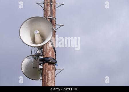 Tannoy-Lautsprecher für Beschallungssysteme, die an einem hölzernen Telegrafenmast befestigt sind, der vor dem wolkigen, grauen Himmel steht. Ballycastle, Großbritannien - 24. August 2024. Stockfoto