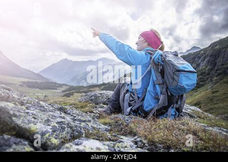 Bergsteiger mit Rucksack sitzt auf dem steinigen Boden und tun eine zeigende Geste Stockfoto