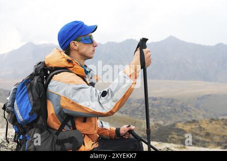 Ein einsamer Tourist mit Rucksack und Stöcken für Bewegung in den Bergen. In Sonnenbrille und mit Rucksack ruhen Sidiya auf einem Stein Stockfoto