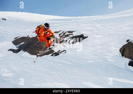 Ein Skirennläufer springt von hohen Felsen in den Bergen. Flusspulver aus dem Schnee hinter dem fliegenden Athleten Stockfoto