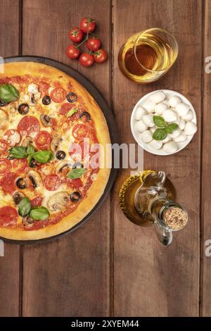 Overhead Foto von Pepperoni Pizza mit Glas Weißwein, Olivenöl, Tomaten und Käse mozzarellini, Schuß von oben auf dunklen rustikalen backgro Stockfoto