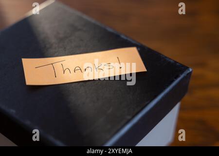 Eine Box mit einer Notiz mit der Aufschrift „Danke“, auf der ein Lichtstrahl auf der Notiz leuchtet. Stockfoto