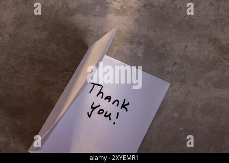 Eine Person schreibt eine Dankesnotiz auf ein Blatt Papier. Die Notiz befindet sich auf einem Holztisch und die Person schreibt sie mit einem Marker. Szene ist positiv Stockfoto
