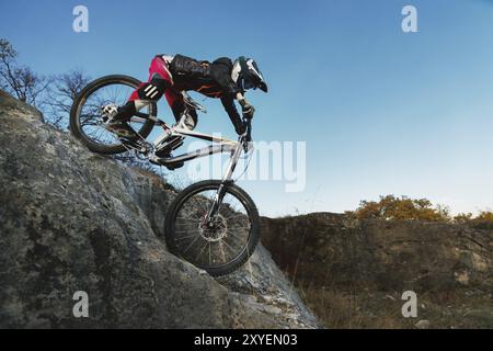 Ein junger Fahrer auf einem MTB-Fahrrad kommt von einer Klippe gegen einen blauen Himmel. Die Abfahrt beim Radfahren ist eine Geschwindigkeit bergab vom Berg auf einem Fahrrad Stockfoto