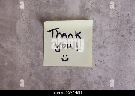 Ein Dankeschön steht auf einem Blatt Papier. Die Nachricht lächelt und sagt: „Danke!“ Darauf Stockfoto