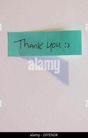 Eine blaue Haftnotiz mit den Worten „Danke“. Der Bezugshinweis wird mit Klebeband an einer weißen Wand oder Oberfläche befestigt Stockfoto