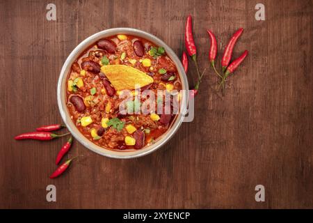 Chili con Carne, traditionelles mexikanisches Gericht, von oben auf einem dunklen rustikalen Holzhintergrund mit einem Nacho-Chip, roten Chilischoten und einem Platz für Stockfoto