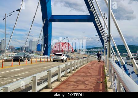 Sokcho, Südkorea - 28. Juli 2024: Ein Radfahrer und Fahrzeuge überqueren die Seorak Grand Bridge und fahren in Richtung der roten Bögen der Geumgang Grand Bridge. Stockfoto