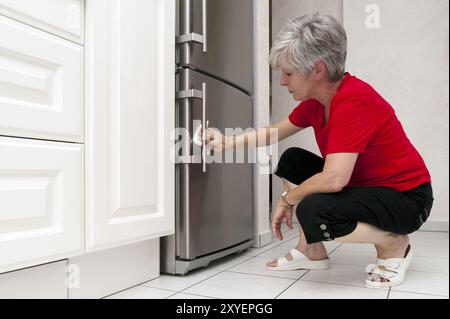 Frau hockt in der Küche und reinigt den Kühlschrank Stockfoto