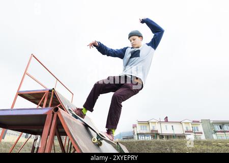 Teenager Skater in Hoodie Sweatshirt und Jeans gleiten über ein Geländer auf einem Skateboard in einem Skatepark, Weitwinkel Stockfoto