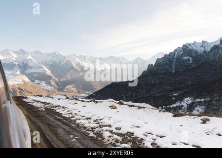 Ein Blick von der Fahrertür des SUV auf eine ländliche Landstraße mit Schmutz und einem Tal von Bergen in der Ferne. Das Konzept des Fahrens auf off-r Stockfoto