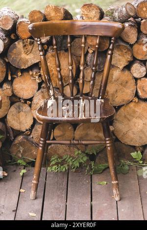 Alter Vintage Stuhl aus Holz auf dem Hintergrund von Holzscheite Brennholz Stockfoto